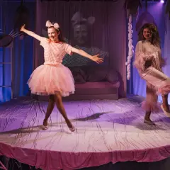 Dwie aktorki w bajkowych strojach bawią się na scenie. Jedna w różowej tiulowej spódnicy, druga w satynowym piżamie. To wesołe przedstawienie teatralne dla dzieci.