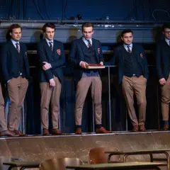 Sześciu młodych mężczyzn w szkolnych mundurkach stoi na scenie.