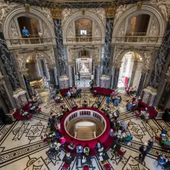 Wnętrze muzeum historii sztuki w Wiedniu z ludźmi przy stolikach i rzeźbą w centrum.