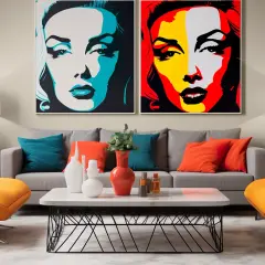 Dwa wyraziste obrazy akrylowe pop art z portretami kobiet, dominują w nowoczesnym salonie z pomarańczowymi fotelami i szarą kanapą.