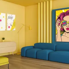 Nowoczesny salon z niebieską kanapą i żółtymi akcentami. Na ścianie wiszą kolorowe pop art obrazy, w tym portret kobiety w okularach.
