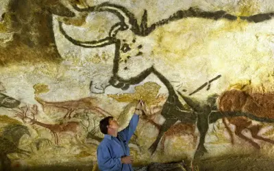 Człowiek bada prehistoryczne malowidła z Lascaux, dotykając pędzlem skalnej ściany z wizerunkami zwierząt.