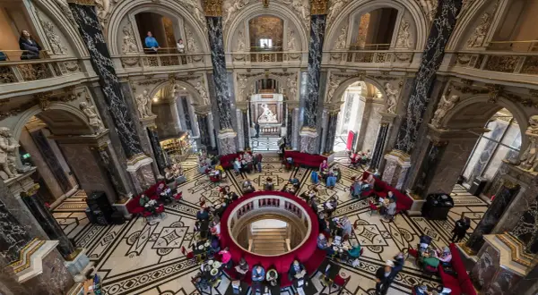 Wnętrze muzeum historii sztuki w Wiedniu z ludźmi przy stolikach i rzeźbą w centrum.