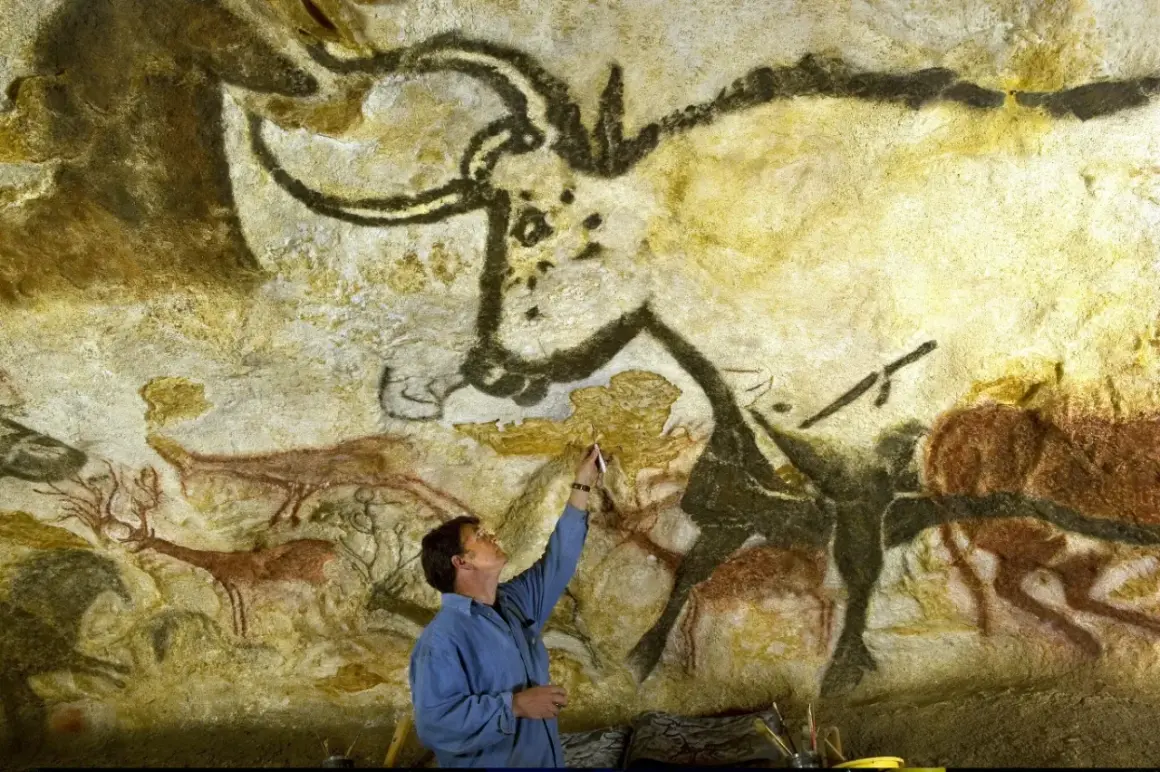 Człowiek bada prehistoryczne malowidła z Lascaux, dotykając pędzlem skalnej ściany z wizerunkami zwierząt.