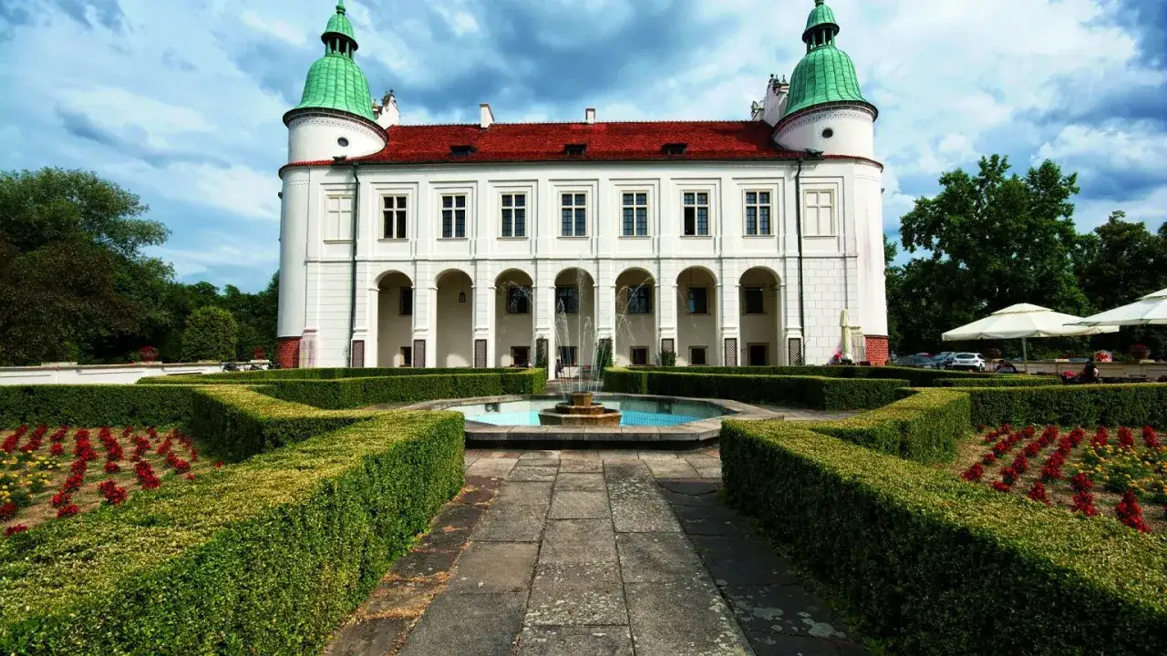 Pałac z arkadowym podcieniem i fontanną, ogród z żywopłotami i rabatami kwiatowymi. Klasyczne cechy sztuki renesansowej widoczne w architekturze.