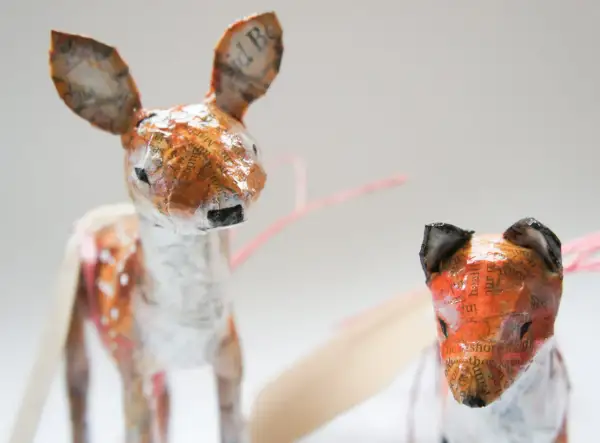 Urocze figurki z papier mache: jelonek w plamki i lis. Ich uszy zdobią fragmenty tekstu.